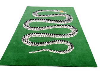 May include: A green rectangular rug featuring a large, stylized snake design. The snake is depicted in white with black markings, and a yellow accent on its head. The rug is a decorative home accent.