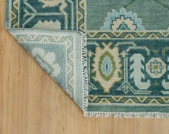 May include: Close-up of the back side of a teal blue rug with a white fringe. The rug has a geometric pattern with floral motifs.