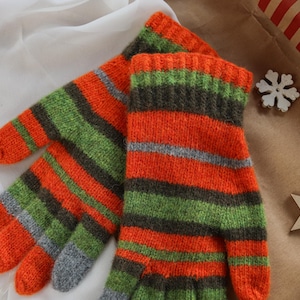 May include: A pair of knitted gloves with orange, green, and gray horizontal stripes. The gloves are made of a soft, textured yarn and have a ribbed cuff. The gloves are designed for warmth and comfort.