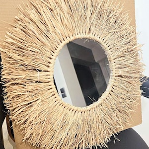 Peut inclure: Un miroir rond avec un cadre en paille tressée naturelle. Le cadre est épais et a une texture en frange.