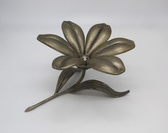 Op de afbeelding: Een bronzen metalen bloemensculptuur. De bloem heeft zes bloemblaadjes, een stengel en twee bladeren. De bloemblaadjes zijn lichter van kleur dan de stengel en de bladeren. Het is waarschijnlijk een decoratief item.