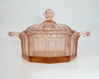 May include: A pink glass butter dish with a lid and two handles. The dish has a fluted design and is made of clear glass with a pink tint.
