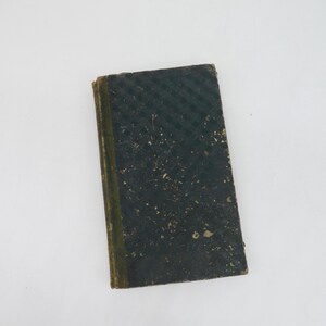 K&ouml;nnte beinhalten: Ein kleines, antikes Buch mit einem dunkelgr&uuml;nen Einband. Der Einband hat ein strukturiertes, diagonal gestreiftes Muster und weist Gebrauchsspuren auf. Der Buchr&uuml;cken ist hellgr&uuml;n. Das Buch ist rechteckig und scheint alt zu sein.