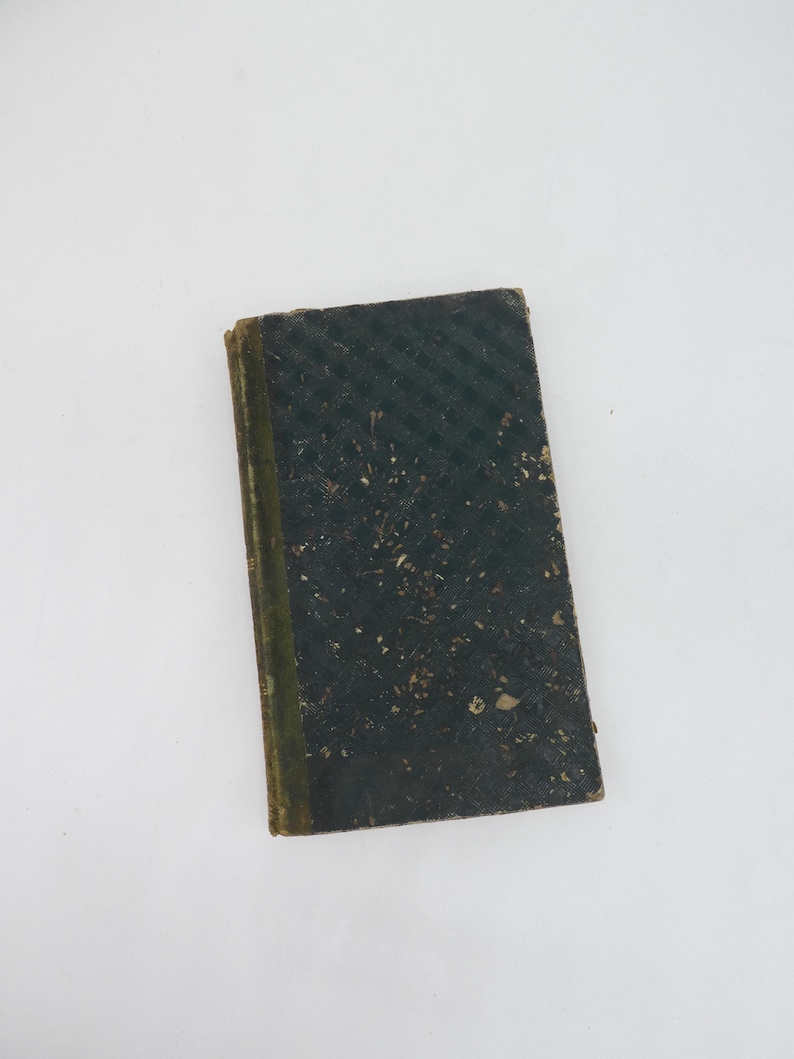K&ouml;nnte beinhalten: Ein kleines, antikes Buch mit einem dunkelgr&uuml;nen Einband. Der Einband hat ein strukturiertes, diagonal gestreiftes Muster und weist Gebrauchsspuren auf. Der Buchr&uuml;cken ist hellgr&uuml;n. Das Buch ist rechteckig und scheint alt zu sein.