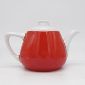 Peut inclure: Une théière en céramique rouge et blanche avec un corps arrondi, une anse incurvée et un bec verseur. Le couvercle est blanc avec une petite poignée. La théière est conçue pour infuser le thé et convient à un usage en cuisine.