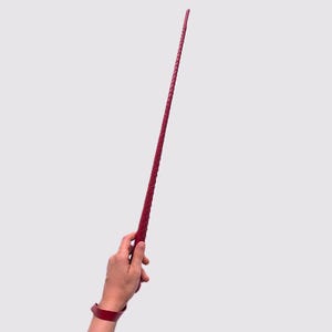 Pode incluir: Um chicote de couro vermelho com um design trançado.