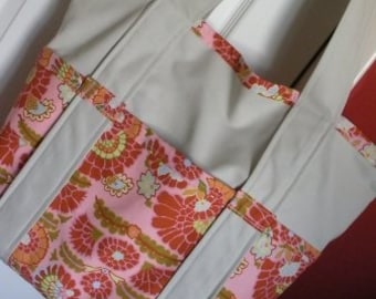 May include: A beige tote bag with a floral pattern in shades of pink, red, and orange. The bag has a large main compartment and two smaller pockets on the front.