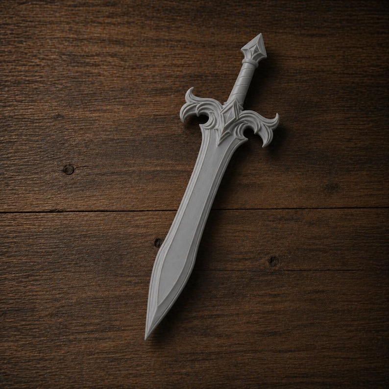 May include: A gray decorative sword with an ornate hilt and a pointed blade. The sword is made of a light gray material and is set against a dark wood background. The hilt features a diamond-shaped design.