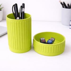 May include: A lime green desk organizer set. The set includes a tall cylindrical pen holder with black pens and a small round dish with two USB drives. The organizer has vertical ridged detailing.