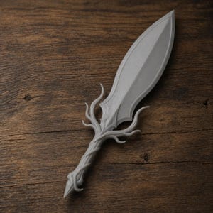 May include: A gray, decorative dagger with a leaf-shaped blade and a handle designed to resemble intertwined branches. The dagger is made of a solid material and rests on a wooden surface.