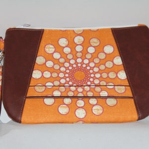 May include: A brown and orange zippered pouch with a white and pink circle pattern. The pouch has a brown leather trim and a detachable wrist strap.