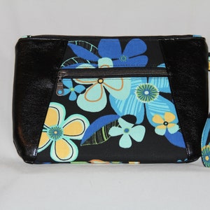 May include: Black zippered clutch with a floral print featuring blue, yellow, and green flowers on a black background. The clutch has a black leather trim and a detachable wrist strap.