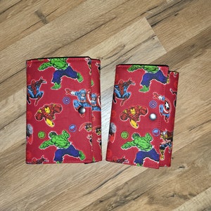 May include: Two red fabric wallets with a superhero print featuring characters like Hulk, Iron Man, Spiderman, and Captain America.