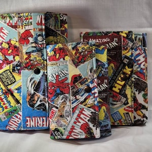 May include: Three fabric wallets featuring a colorful collage of vintage Marvel comic book covers including Iron Man, Spider-Man, Captain America, and The Incredible Hulk. Each rectangular wallet is secured with a small metal snap button closure.