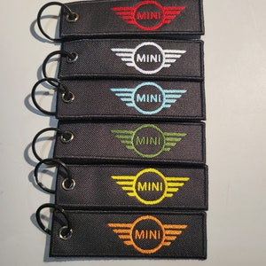 May include: Six black keychains with a silver ring. Each keychain has a white embroidered wing design with a circle in the center. The circles are embroidered in red, white, blue, green, yellow, and orange.