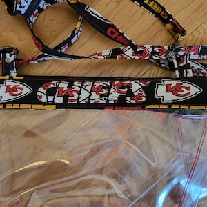 May include: Clear plastic bag with a black and red fabric zipper closure. The fabric has a repeating pattern of the Kansas City Chiefs logo.