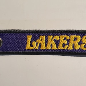 May include: A purple and black keychain with a gold embroidered "LAKERS" logo.