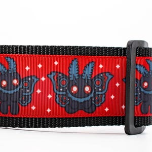 May include: Black dog collar with a repeating pattern of dark blue moth-like creatures on a red background. The collar has black edges and a black plastic buckle. White diamond shapes are scattered across the red background.