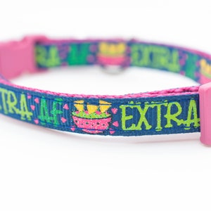 以下が含まれることがあります： 「EXTRA AF」と印刷された青とピンクの猫用首輪。首輪はピンクのバックル付きです。
