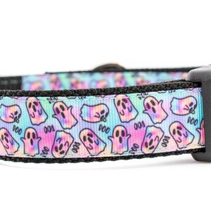 May include: A dog collar with a repeating pattern of cartoon ghosts in pastel colors. The collar has a black plastic buckle and a black trim. The word "Boo" is printed on the collar.