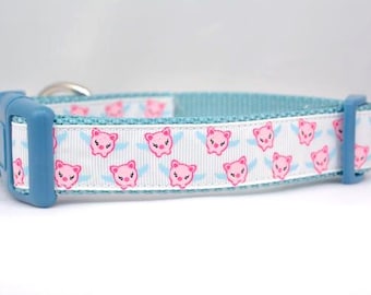 May include: A pet collar featuring a white ribbon overlay with a repeating pattern of pink winged pigs. The collar has a light blue nylon base, a matching light blue plastic side-release buckle, and a silver metal D-ring for attaching a leash.