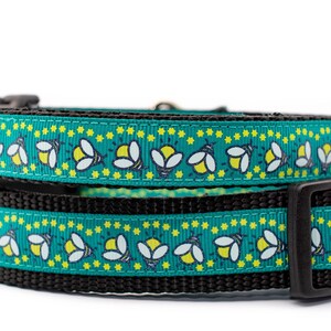 May include: Two dog collars stacked on top of each other. The top collar is teal with a pattern of white and yellow fireflies and yellow stars. The bottom collar is black. Both collars have black plastic buckles.