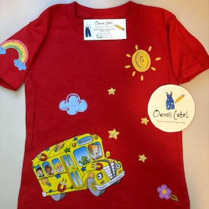 Op de afbeelding: Een rood T-shirt met korte mouwen en een gele schoolbus-afbeelding met de tekst "WAHOO!". Het shirt bevat prints van een regenboog, zon, wolken, sterren en een bloem, samen met een rechthoekig en een rond "Overall Cute!"-label.