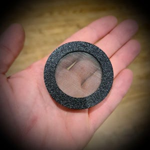 May include: A black round mesh filter with a black outer ring. The filter is made of fine mesh and has a slightly textured surface.