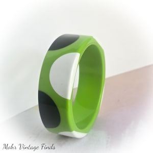 May include: A wide bangle bracelet featuring a vibrant lime green base color with a repeating pattern of large, solid black and white circular polka dots. The bracelet has a smooth, glossy finish and a thick, rounded band construction.