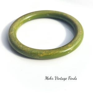 May include: A vintage olive green bangle bracelet. The round bracelet has a marbled design with gold-colored swirls. The text "Mohr Vintage Finds" is at the bottom of the image.