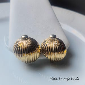 May include: A pair of gold-toned clip-on earrings. Each earring has a ribbed, rounded design with a small, smooth dome on top. The earrings are displayed on a white surface. The text "Mohr Vintage Finds" is visible in the bottom right corner.