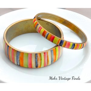 May include: Two gold bangles with colorful striped enamel. The stripes are in shades of pink, orange, yellow, green, blue, and white.