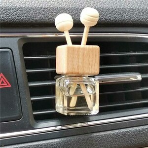 May include: A car air freshener with a clear glass bottle and a wooden top. Two wooden sticks with spherical tops extend from the top. The air freshener is placed on a car's air vent.