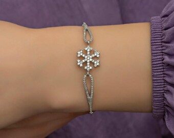 Pode incluir: Um bracelete de prata com um pingente de floco de neve adornado com pedras de zircônia cúbica transparentes. O bracelete é feito de uma corrente delicada e tem um design simples.