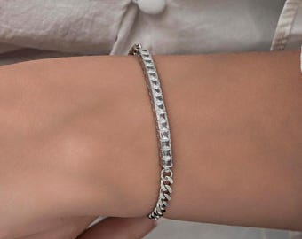 Op de afbeelding: Een zilveren armband met een kettingschakelontwerp en een rij vierkante stenen.