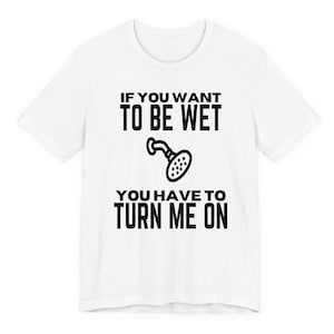 May include: White t-shirt with black text and a showerhead graphic. The text reads: "IF YOU WANT TO BE WET YOU HAVE TO TURN ME ON."