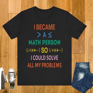 May include: Black t-shirt with colorful text: "I BECAME > A ≤ MATH PERSON (√÷x+-) SO (√÷x+-) I COULD SOLVE ALL MY PROBLEMS." Includes blue jeans and a pair of sneakers.