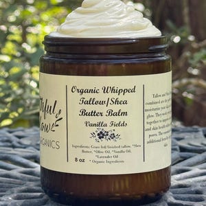 May include: A brown glass jar with a white label that reads "Organic Whipped Tallow/Shea Butter Balm Vanilla Fields". The jar contains a white, whipped cream-like substance. The label also lists the ingredients and size: 8 oz. Organic Ingredients.