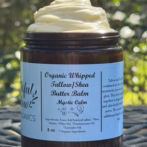 May include: A brown glass jar with a white label that reads "Organic Whipped Tallow/Shea Butter Balm Mystic Calm". The label also lists the ingredients: Grass fed/finished tallow, Shea Butter, Olive Oil, Frankincense Oil, Lavender Oil. The jar contains a white, whipped balm and is 8 oz.