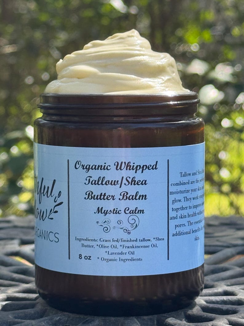 May include: A brown glass jar with a white label that reads "Organic Whipped Tallow/Shea Butter Balm Mystic Calm". The label also lists the ingredients: Grass fed/finished tallow, Shea Butter, Olive Oil, Frankincense Oil, Lavender Oil. The jar contains a white, whipped balm and is 8 oz.