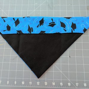 May include: A blue and black fabric triangle with a graduation cap pattern. The fabric is folded in half and the edges are sewn together.