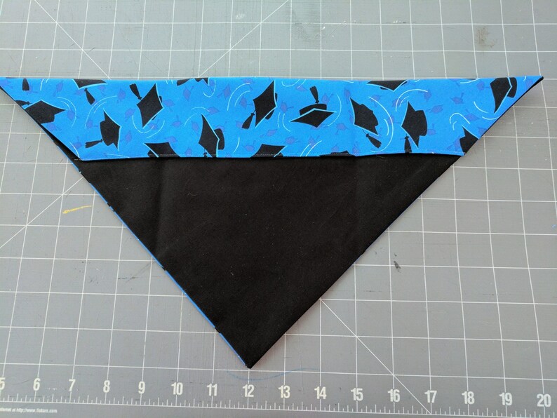May include: A blue and black fabric triangle with a graduation cap pattern. The fabric is folded in half and the edges are sewn together.