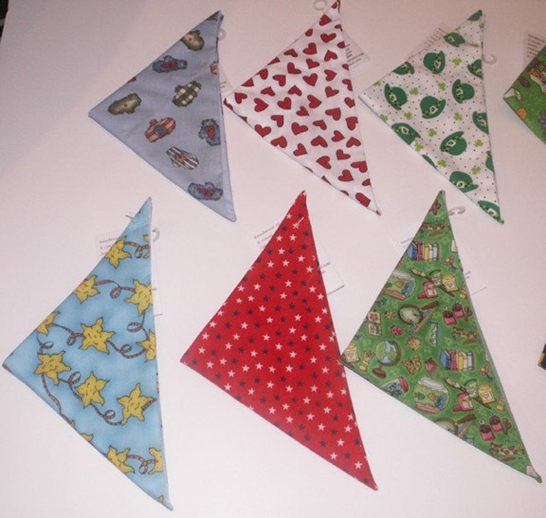 May include: Assortment of triangular bandanas in various patterns. Designs include red hearts on white, green shamrocks, blue with yellow stars, red with white stars, and a green print with books and globes. Each bandana has a small tag attached.