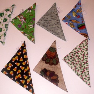 May include: A collection of triangular bandanas with various patterns. Designs include candy corn on black, a turkey, green shamrocks, a bunny with carrots, Japanese script, and a food-themed pattern with hot dogs. The bandanas are likely for pets.