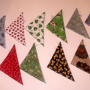 May include: A collection of triangular fabric ornaments with various patterns. Designs include hearts, stars, candy corn, and holiday motifs. Each ornament has a small loop for hanging.