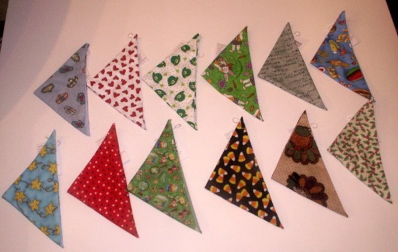 May include: A collection of triangular fabric ornaments with various patterns. Designs include hearts, stars, candy corn, and holiday motifs. Each ornament has a small loop for hanging.