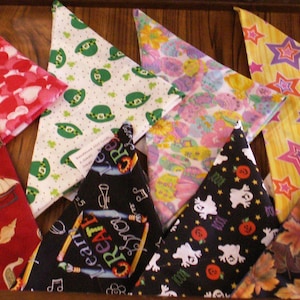 May include: A collection of colorful triangular bandanas with various patterns, including candy canes, hearts, shamrocks, stars, and flags. The bandanas are arranged on a wooden surface, showcasing a variety of festive and seasonal designs.