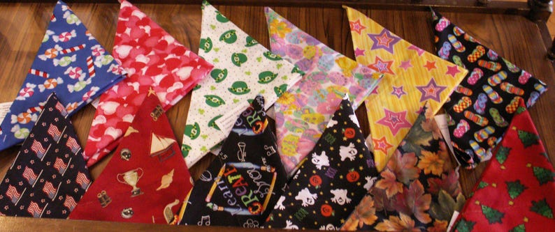May include: A collection of colorful triangular bandanas with various patterns, including candy canes, hearts, shamrocks, stars, and flags. The bandanas are arranged on a wooden surface, showcasing a variety of festive and seasonal designs.
