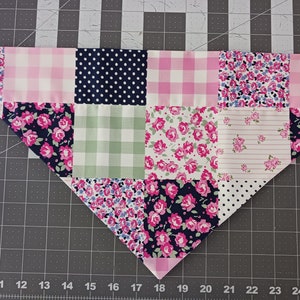 May include: A triangular pet bandana featuring a patchwork design of various fabric squares. The patterns include pink and white gingham, navy blue with white polka dots, light green gingham, and floral prints with pink roses on navy and white backgrounds.