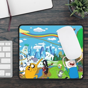 May include: A colorful mousepad featuring characters from the animated series Adventure Time. The design includes Finn the Human, Jake the Dog, Princess Bubblegum, and other characters from the show. The mousepad is a bright blue with a rainbow, clouds, and a snowy mountain landscape.